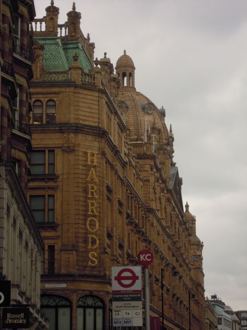 This image features a historic building in Knightsbridge with intricate architectural details and ornate decorations. A large, vertical sign reading 'HARRODS' is prominently displayed along the side o